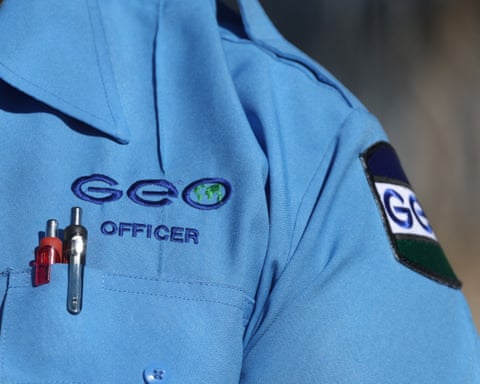 A closeup of the chest pocket of a person wearing a blue work shirt, with the words “Geo officer” embroidered above a couple pens.