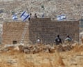 Israeli settlers fly flags over a stone building in an arid landscape