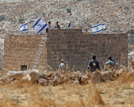 Coloni israeliani issano bandiere su un edificio in pietra in un paesaggio arido