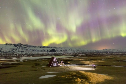 An aurora hunter photographs a traditional house lit by the northern lights.