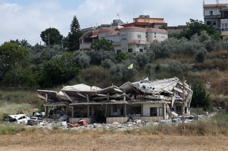 A destroyed building in a green space at the edge of a village.