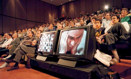 An audience watching a stage with a screen of Kasparov and a screen of the chess game