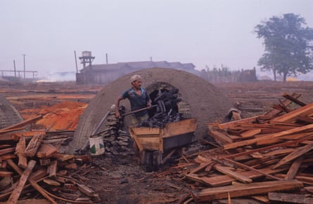 Um homem retirando carvão de um forno em forma de iglu com pilhas de madeira de cada lado