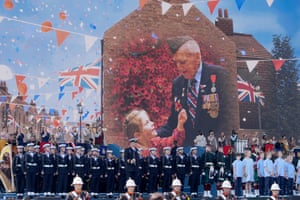 Rows of navy personnel and children in front of images projected on to a large screen on the side of a house