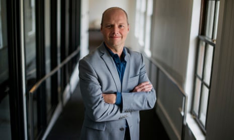 a suited sebastian thrun in shirt collars standing with his arms folded in a corridor