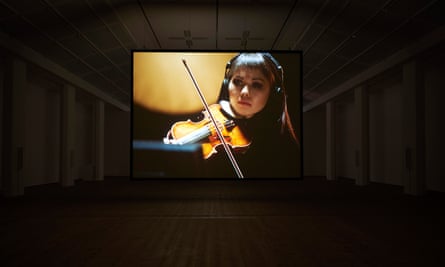 A screen showing violinist Leila Akhmetova in the middle of a hall of speakers.