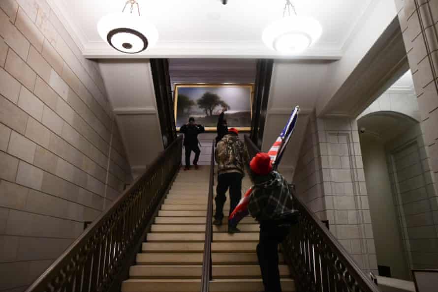 Trump supporters, one holding an American flag, wander a stairway in the US Capitol building.