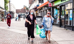 Two women in face masks carrying shopping bags along a pedestrianised shopping street