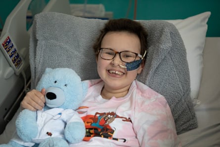 Alyssa, a 13-year-old girl, in a hospital bed holding a teddy bear and smiling