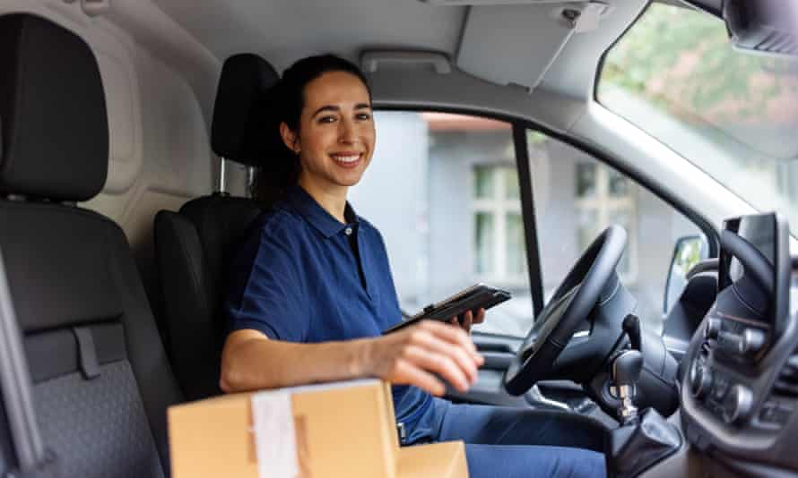 Happy female courier sitting in delivery van and looking at camera. Woman delivery worker sitting in delivery van holding digital tablet and parcel boxed on front seat.
