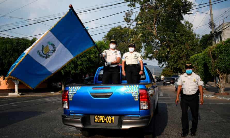 Police officers wearing face masks wave the Guatemalan flag from a police truck on the streets of the Chacara neighborhood during a partial curfew ordered by the government, in Guatemala City on 27 March.