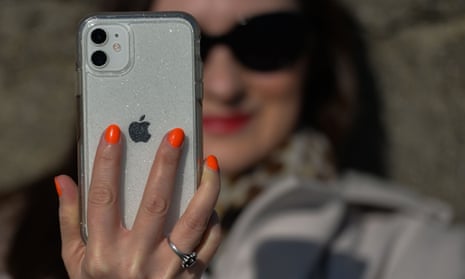A woman with bright orange fingernails holds a silver iPhone