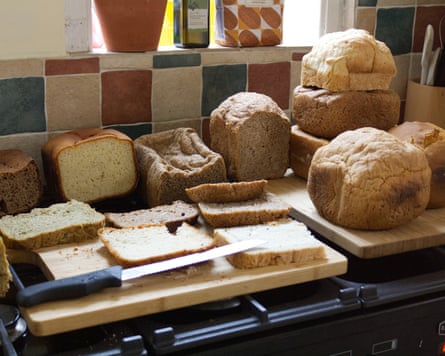 Several loaves of homemade bread, some sliced, sit on wooden boards and a stovetop, with a knife beside sliced pieces