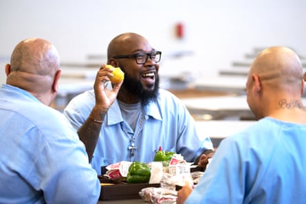 a man holding a pear and smiling while he sits pinch 2 different men successful beforehand of repast trays