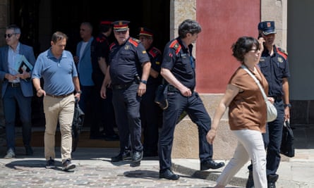 Police officers in navy and red uniforms emerge from a doorway into a sunny street