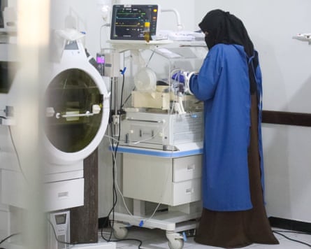 A healthcare worker attends to a baby in an incubator in a neonatal intensive care unit