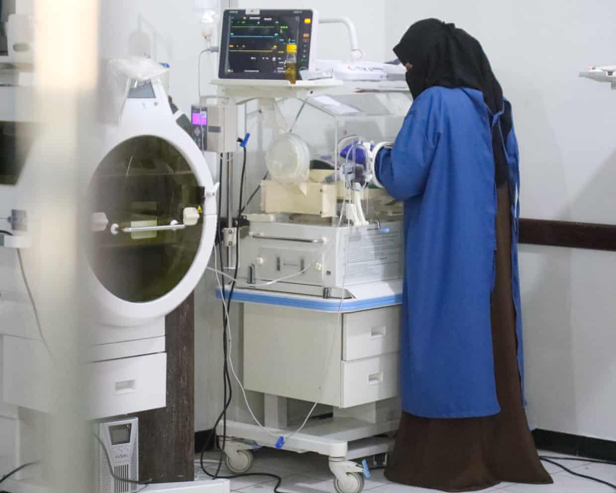 A healthcare worker attends to a baby in an incubator in a neonatal intensive care unit