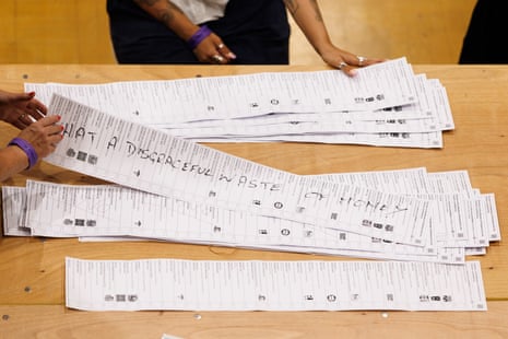 The words ‘What a disgraceful waste of money’ have been written on a ballot paper that is being sorted through among a pile on a table