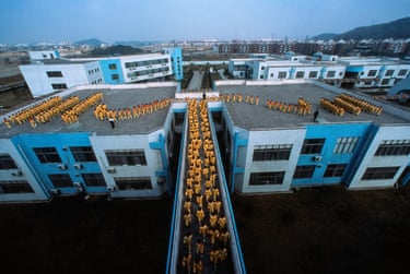Aerial photograph of dozens of students in yellow on rooftops filing over a bridge