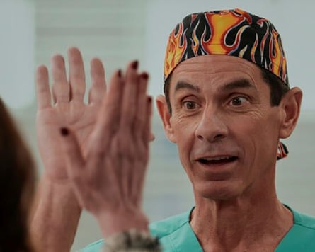 A character from Scrubs, The Todd, gives a high-five to another character. He is dressed in blue scrubs with a cap over his head printed with flames.