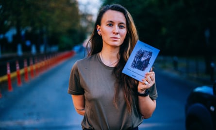 Soldier and poet Yaryna Chornohuz, dressed in uniform, stands in a road in Kyiv holding her book of poems.