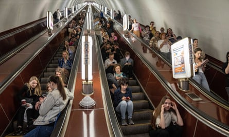 Dozens of people sit and stand on a stationary escalator in a Kyiv metro station