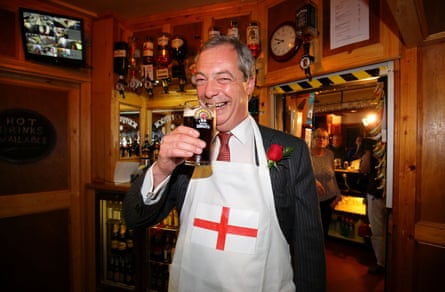 Nigel Farage wearing a white apron with an English flag on it and holding up a pint of bitter while standing in a pub