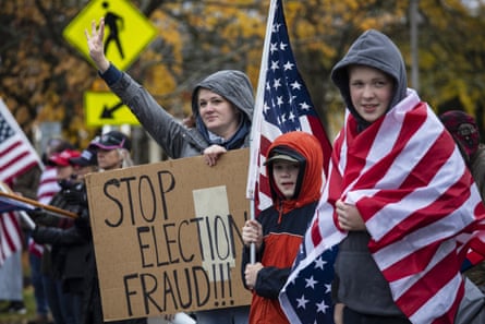 Two young children holding big American flags stand next to a woman holding a sign that reads ‘Stop election fraud!!!’
