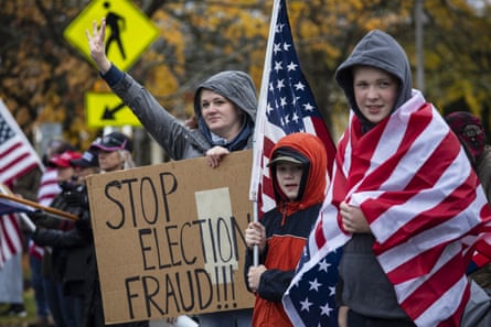 Twee jonge kinderen met grote Amerikaanse vlaggen staan naast een vrouw met een bord met de tekst 'Stop verkiezingsfraude!!!'