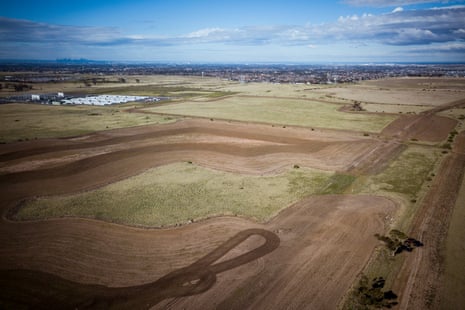 An aerial view of Plumpton farmland with a green crop patch, distant housing and city skyline beyond