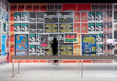 A person inspects a wall plastered with posters for bands such as Fugazi, Mudhoney and the Offspring