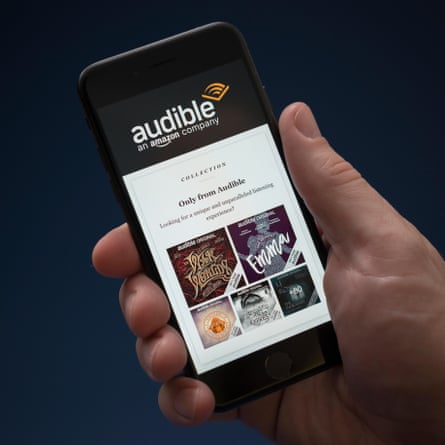 A man looks at his iPhone which displays the Audible logo