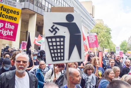 Group of people, one wearing a keffiyah, and holding signs saying ‘refugees welcome’ and someone putting a swastika in the bin