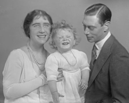 A black and white photo of Queen Elizabeth II as a baby being held by her mother with her father next to her. All three are smiling.
