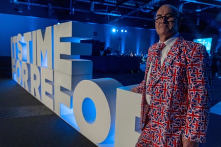 George Preston stands next to a Reform UK sign wearing a suit covered in union flags