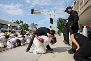 Performers acting as law enforcement agents and as immigration detainees, who are kneeling and dressed in white
