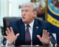 Donald Trump gesturing as he is sat down at a desk in the Oval Office
