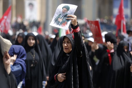Woman in black chador holds image of former supreme leader in the air with one hand amid other mourners
