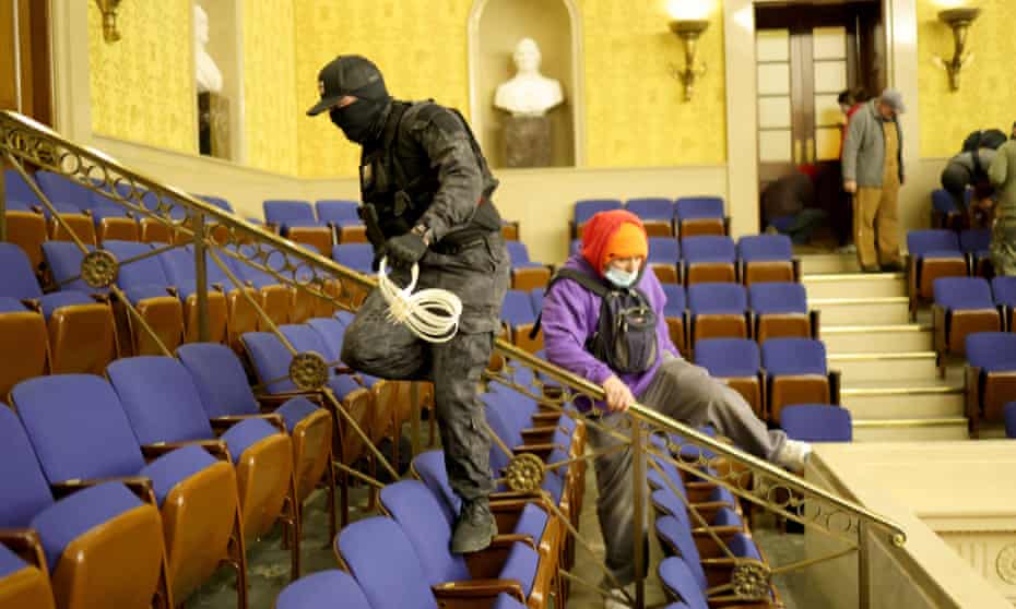 Two rioters climbing over  chairs in the Senate chamber, one with an armful  of plastic restraints