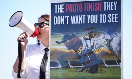 An animal rights activist with a loudhailer stands next to a poster  showing a horse breaking its leg in a race
