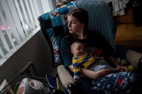 A woman cradles her baby on a rocking chair inside