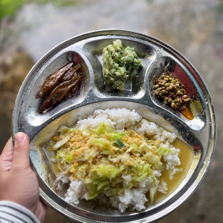 A child’s hand holds a metal plate with four sections and food in each