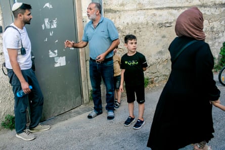 Zohar Rajabi (C) stands talking to a Jewish settler outside the door of a house. A child is stood alongside Rajabi