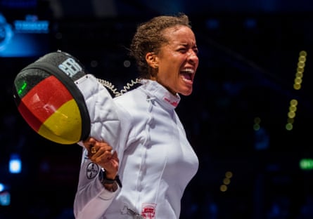 A woman cheering, holding a fencing mask