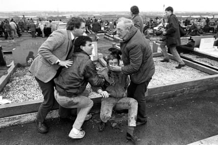 McGuinness and others help a man injured in a deadly gun and bomb attack at an IRA funeral in Belfast in 1988