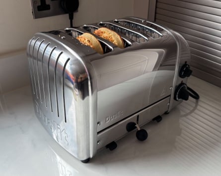 A silver Dualit 4 Slice NewGen Classic Toaster with two crumpets in it on a worktop