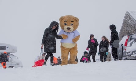 A woman holding a sledge in one hand holds the hand of a person in teddy bear costume