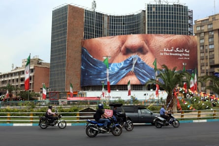 People drive past a billboard with Trump’s lower face gagged by an illustration of the strait of Hormuz