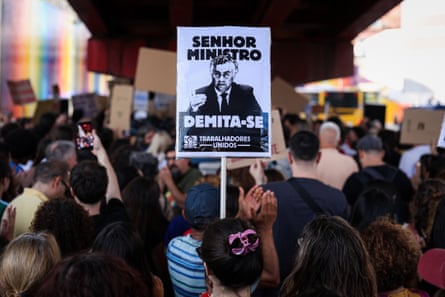 Students protesting outside the education ministry, seen in a crowd from behind, hold signs calling for the education minister’s resignation.