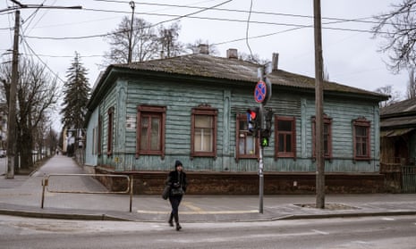 A woman crosses a street near a traditional wooden house in Chernihiv.